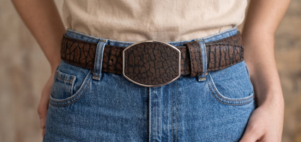 Woman wearing jeans and a brown 30 mm bull neck texture western belt with the shield-shaped buckle of sizes 22 to 32
