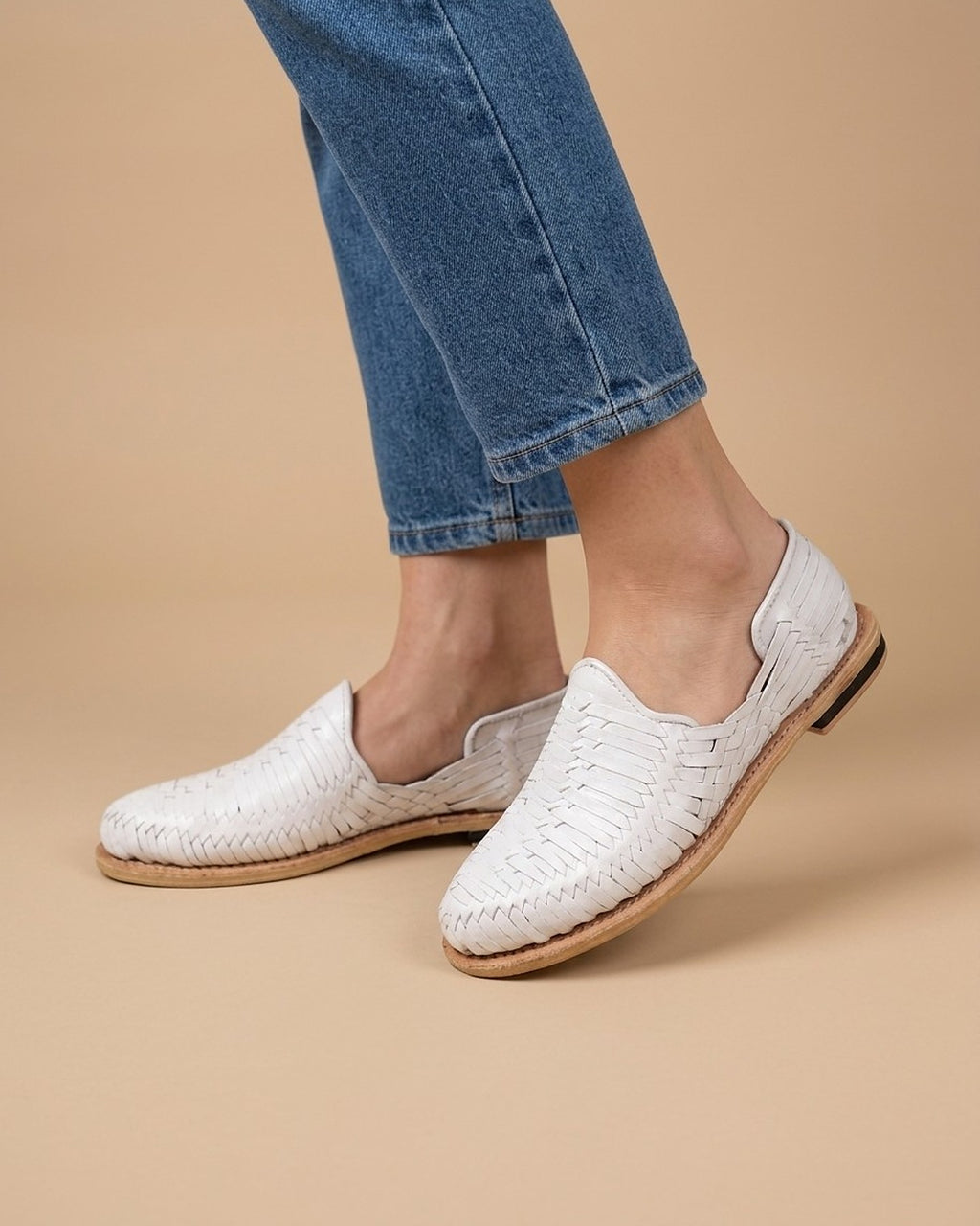 Women's white huarache sandals in hand-woven leather with a closed toe and leather sole, worn with ankle-length jeans; AI-generated lifestyle image