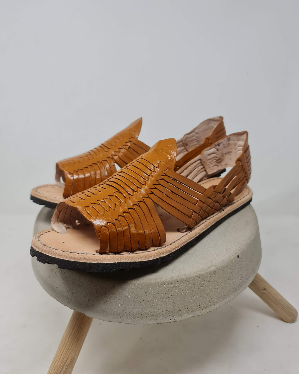Men's honey brown leather huarache sandals on a concrete stool, three-quarter view