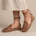 Women's brown Roman huarache sandals worn with a linen skirt: tooled sunflower on the vamp and ties knotted at the ankle