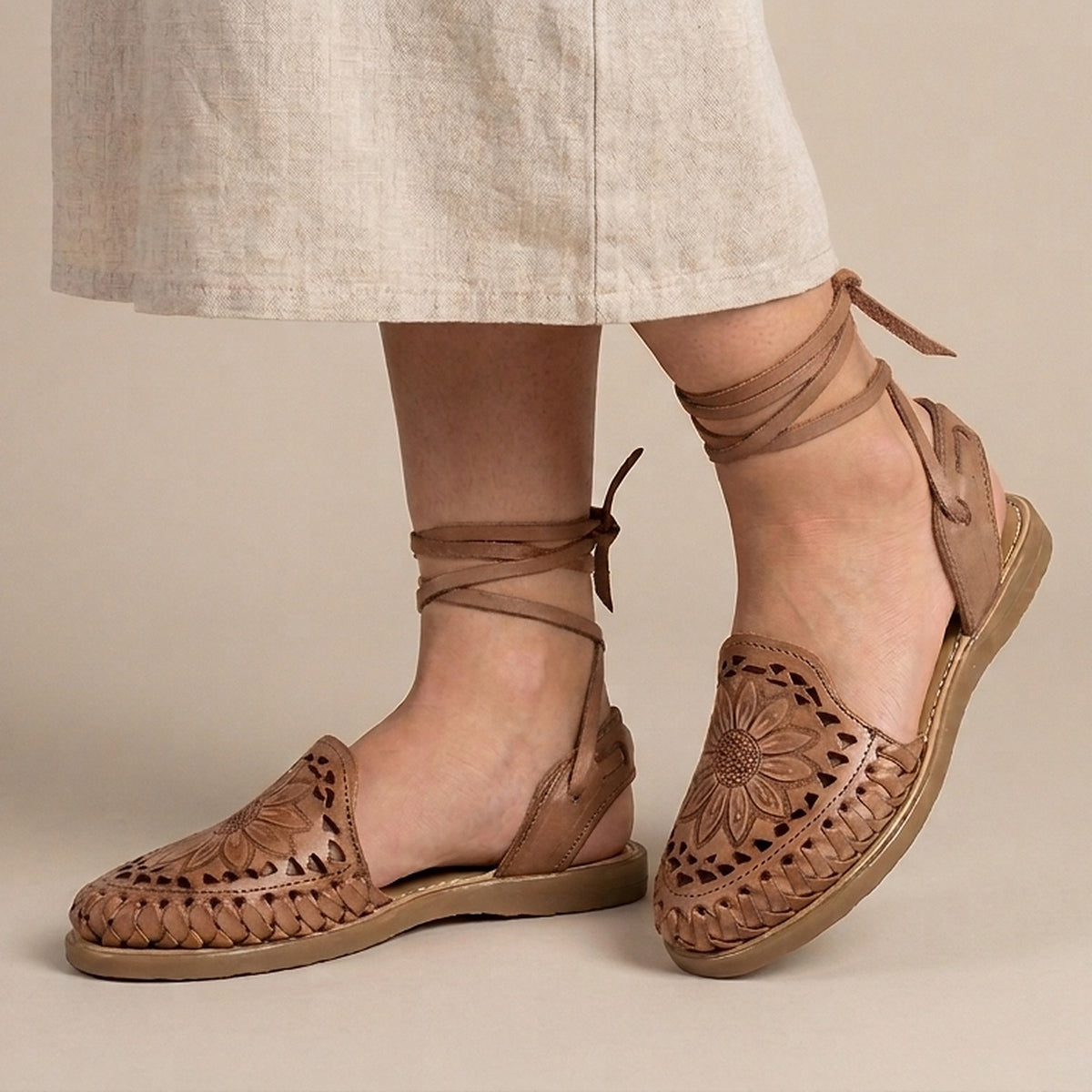 Women's brown Roman huarache sandals worn with a linen skirt: tooled sunflower on the vamp and ties knotted at the ankle