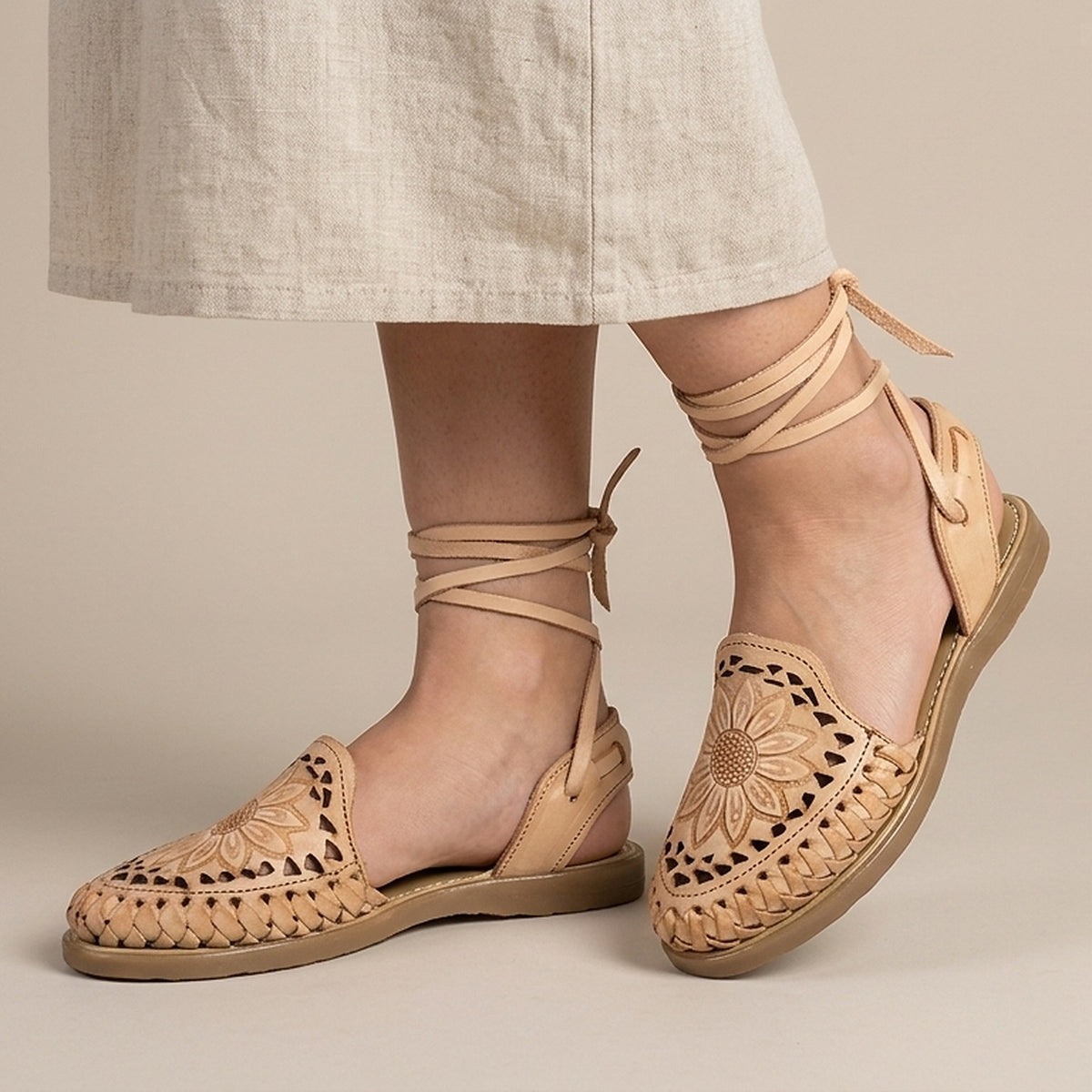 Women's honey Roman huarache sandals worn with a beige linen skirt: tooled sunflower and ties knotted at the ankle