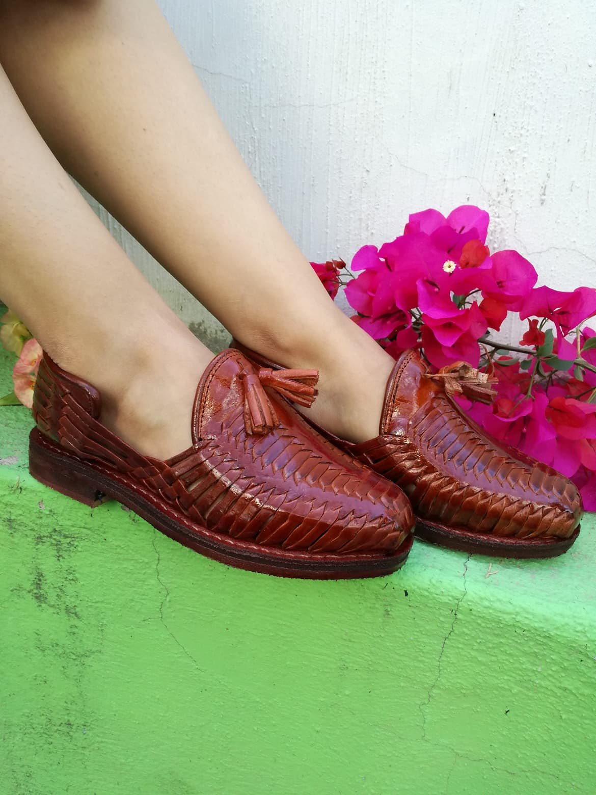 Women's woven huaraches in reddish brown next to bougainvillea