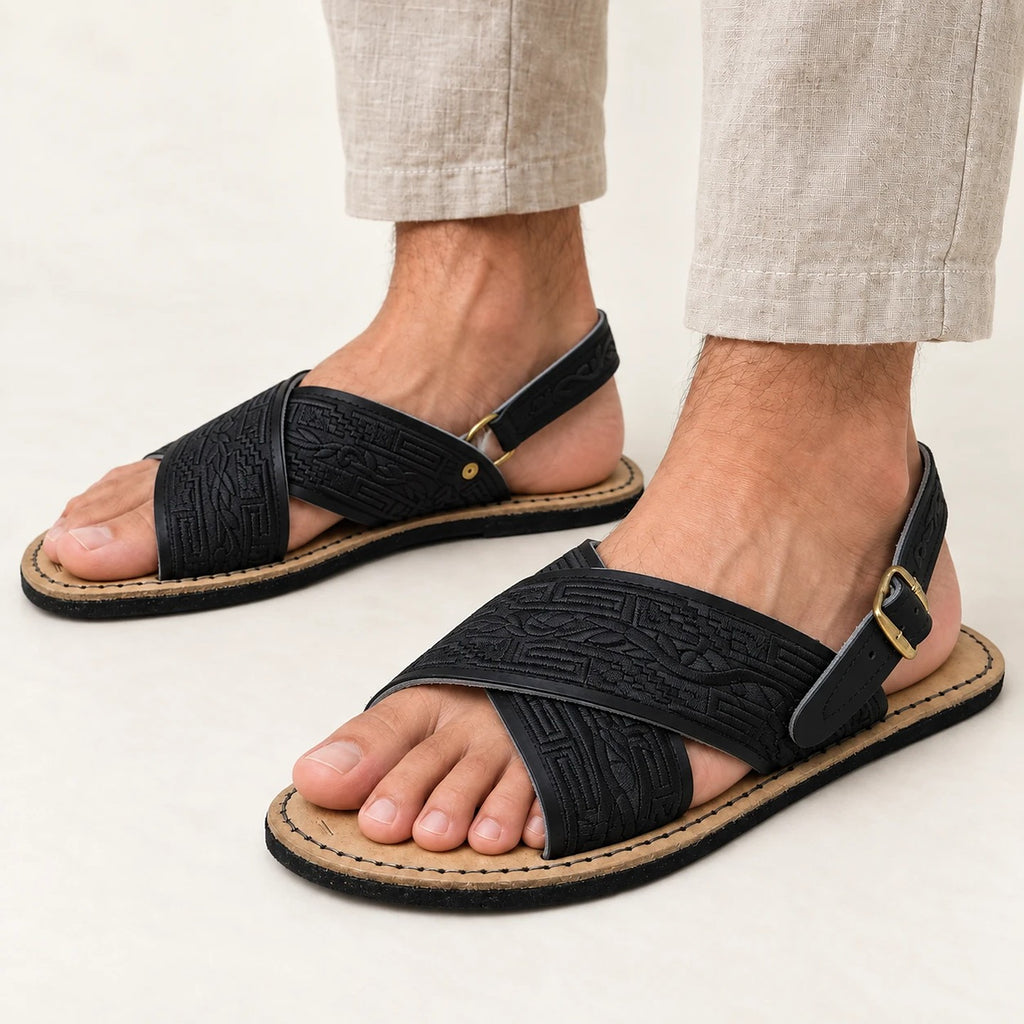 Men's huarache sandals in black with black embroidery and cross straps, worn with linen pants