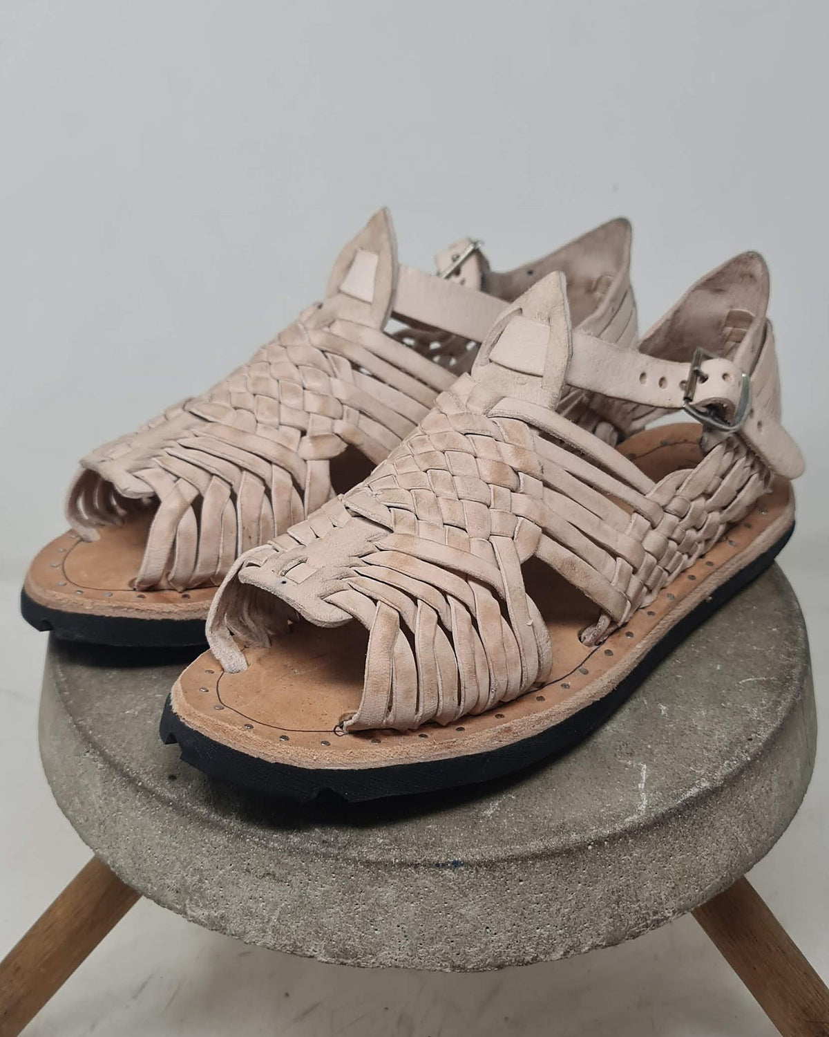 Natural leather huaraches for men on a concrete stool: pachuco weave, ankle strap and buckle, three-quarter view
