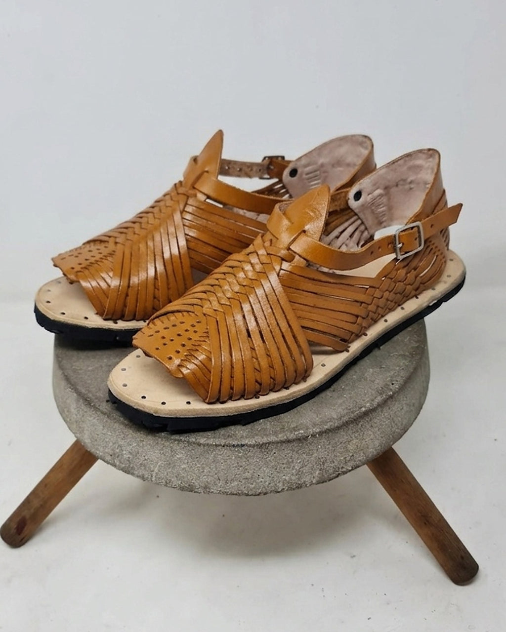 Tan pachuco huaraches for men on a concrete stool: thin woven straps, adjustable buckle and natural leather insole